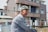 A happy customer, John D., smiling in front of his new home.