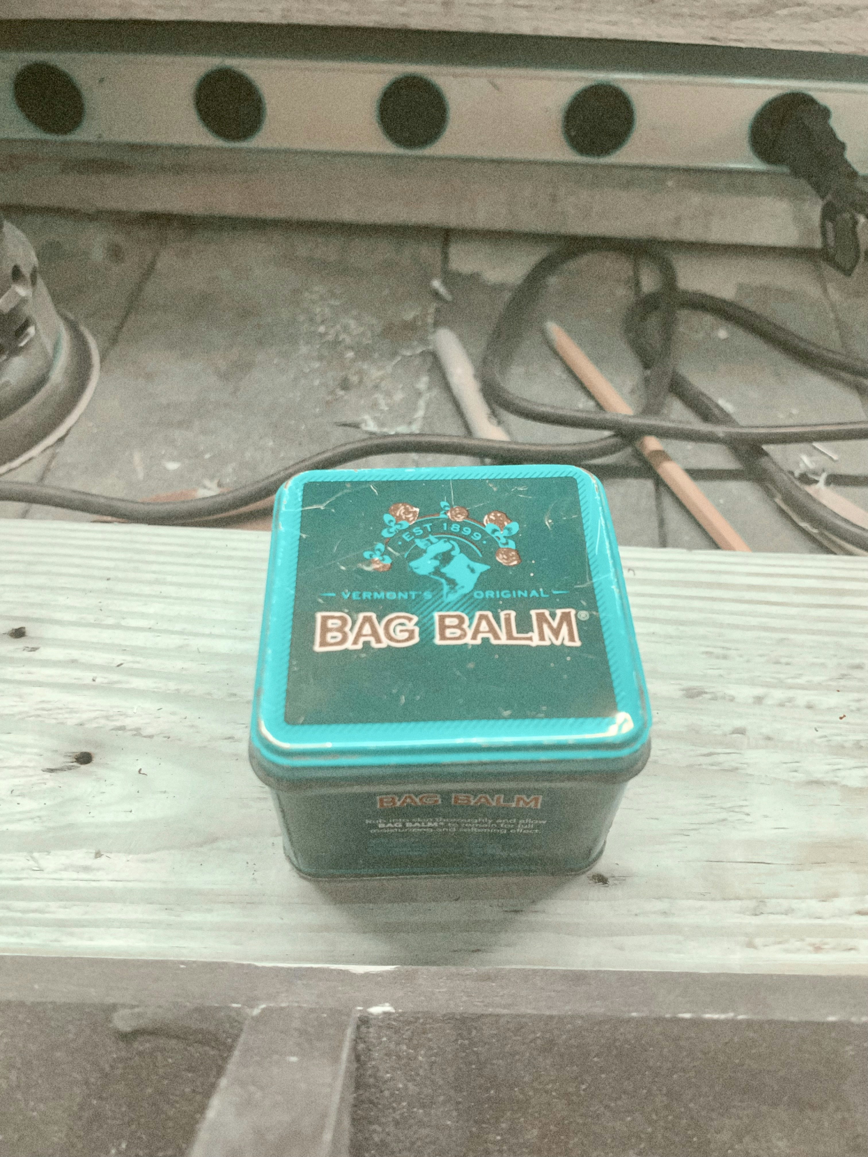 Dark green herbal balm tin surrounded by dried herbs and flowers on dark wooden surface