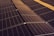 A series of solar panels arranged in rows, capturing sunlight. The panels have a grid-like pattern and are placed on a dark, gravel-covered surface. The symmetry and alignment of the panels give a sense of order and efficiency.