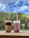 Two cups of bubble tea with lids and straws placed on a ledge, set against a backdrop of lush green hills and a partly cloudy blue sky.