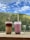 Two cups of bubble tea with lids and straws placed on a ledge, set against a backdrop of lush green hills and a partly cloudy blue sky.