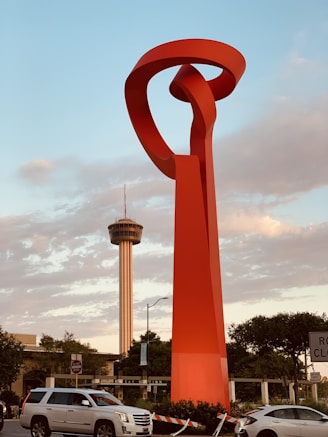 a large red sculpture in the middle of a parking lot