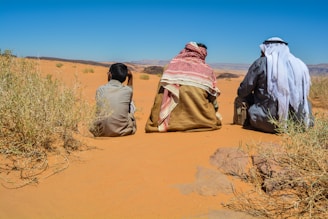 a couple of people sitting on top of a sandy field