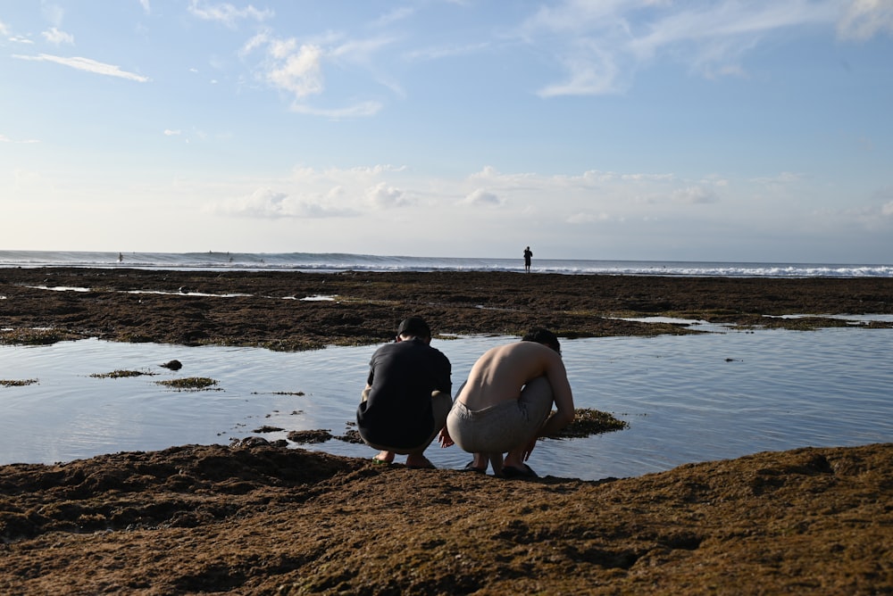 a couple of people sitting on top of a sandy beach