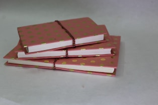 A delicate stack of pastel pink and cream notebooks with floral illustrations on the covers.