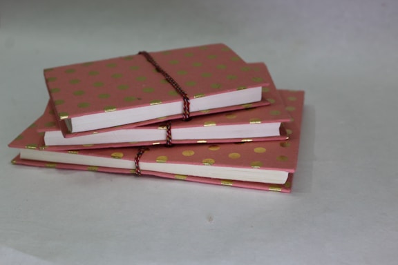 A delicate stack of pastel pink and cream notebooks with floral illustrations on the covers.