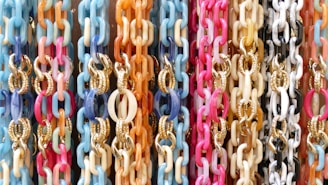 A vibrant display of interlinked chains in various pastel colors, including pink, blue, orange, and white. Some chains feature gold accents.