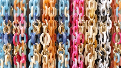A vibrant display of interlinked chains in various pastel colors, including pink, blue, orange, and white. Some chains feature gold accents.