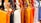 A row of colorful leather handbags displayed in a variety of vibrant shades ranging from orange, black, white, and brown to yellow, red, purple, and pink. The bags are neatly hung by their straps, highlighting their design and metallic buckles.