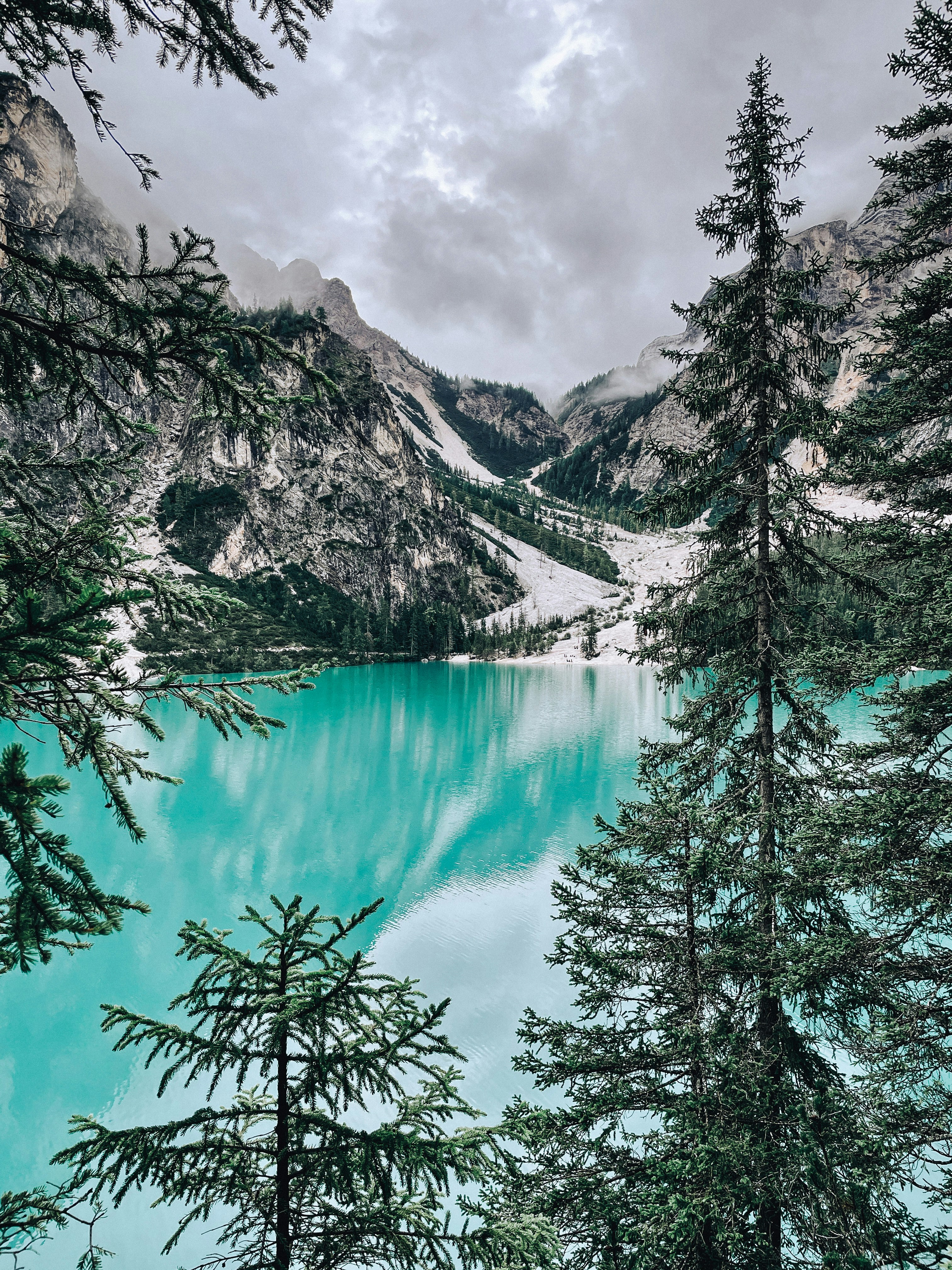 a lake surrounded by trees and mountains under a cloudy sky