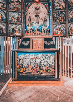 A richly detailed religious or cultural artwork that appears to be an altar piece, featuring numerous figures in religious attire. The central panel depicts a prominent figure with arms outstretched surrounded by others in worship, while the lower section shows a gathering of bearded individuals around a table with mystical imagery. The artwork blends vibrant colors with intricate scenes.