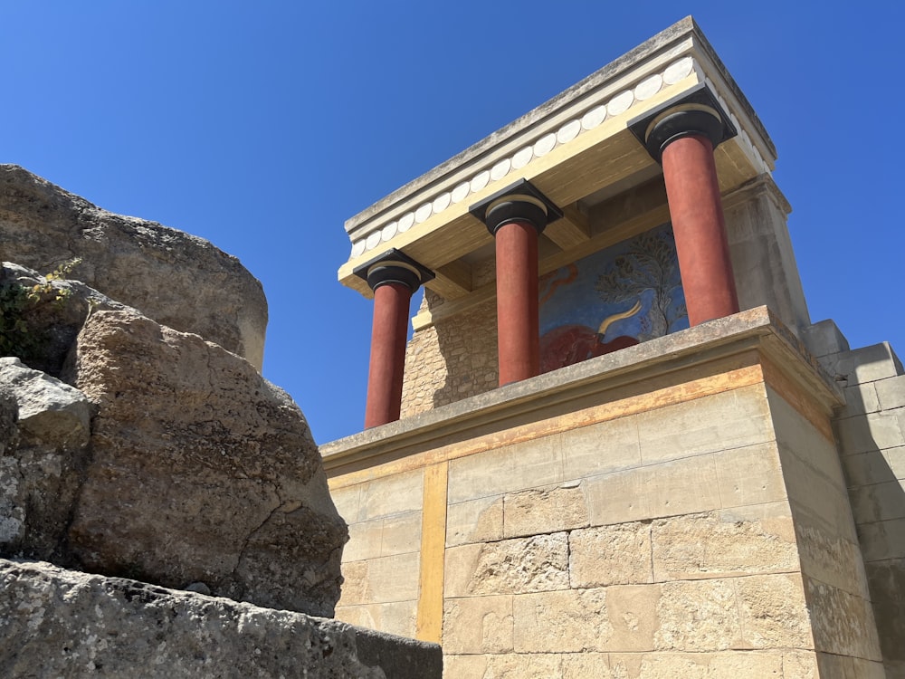 a stone building with two red pillars and a painting on the wall