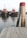 Two red tugboats float side by side in a calm body of water, with a wooden dock prominently in the foreground. A pair of weathered wooden posts with red tops stands near the edge of the dock. The background features greenery and a cloudy sky, contributing to a tranquil setting.