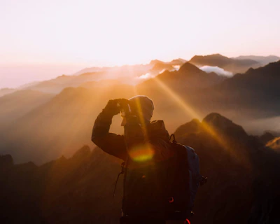 A traveler standing on a mountain peak at sunrise, capturing the breathtaking view with a camera.