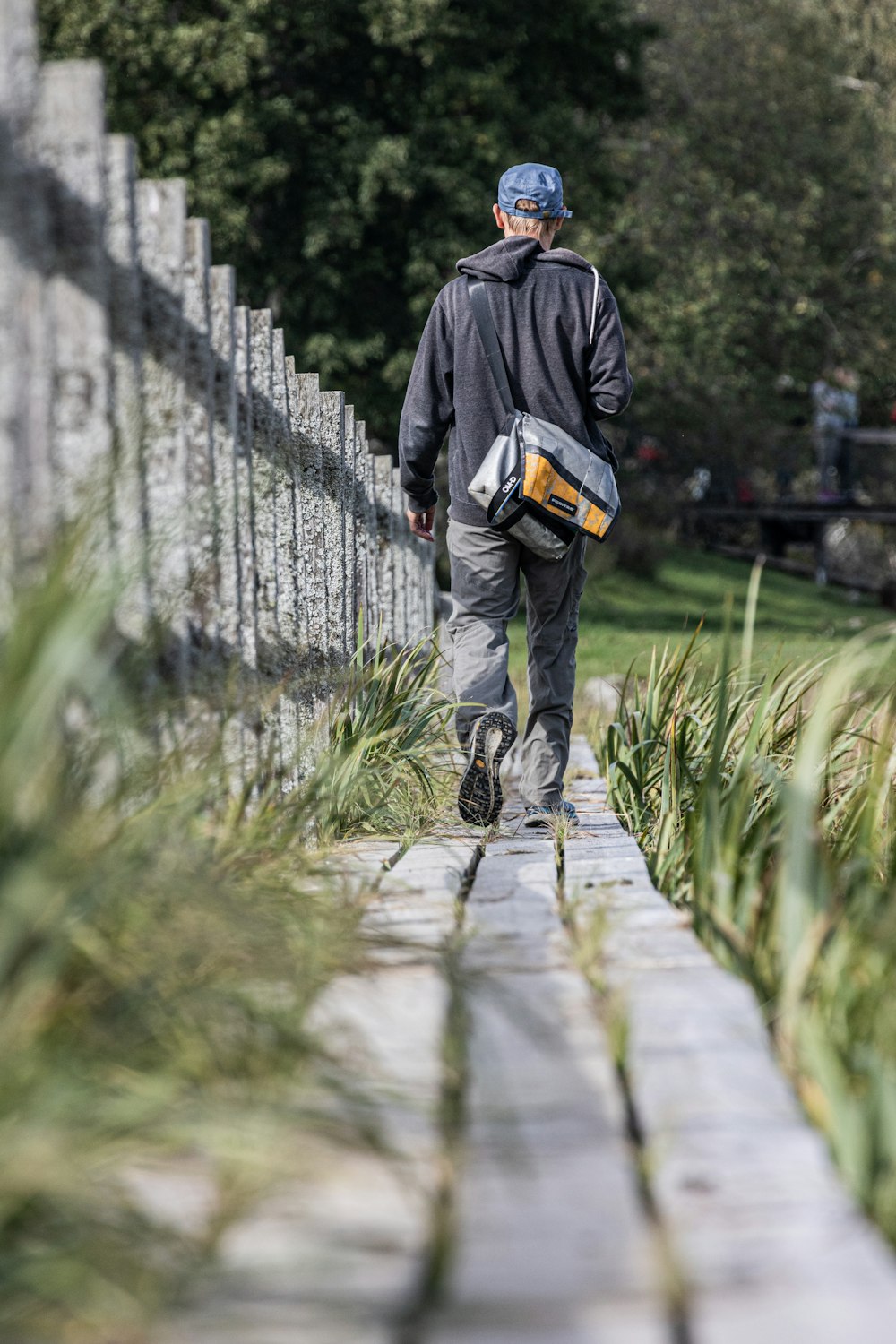 a man walking down a sidewalk next to a fence