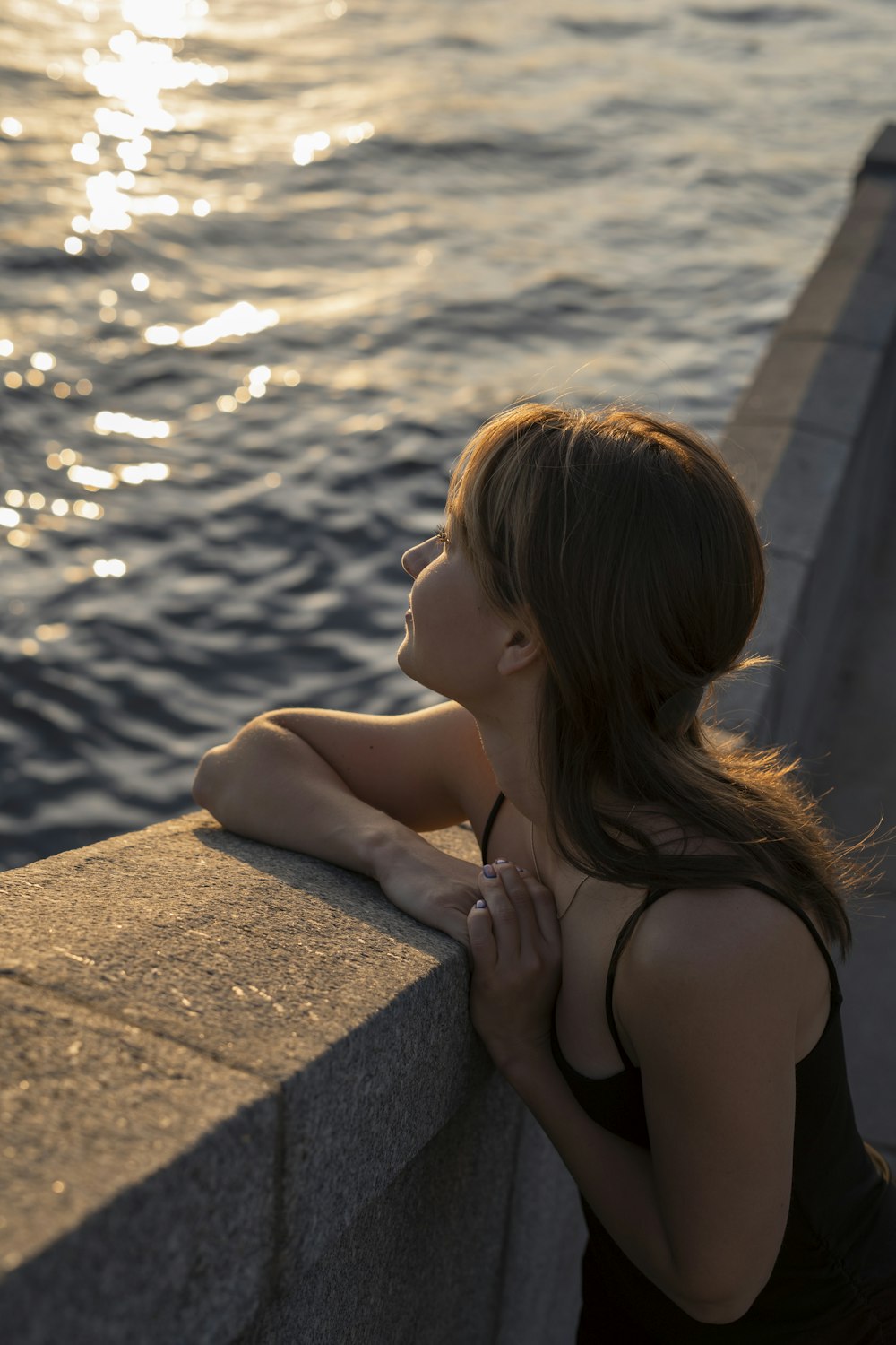 a woman leaning on a wall next to the ocean