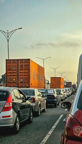 A fleet of container trucks lined up on a busy highway under a clear blue sky.