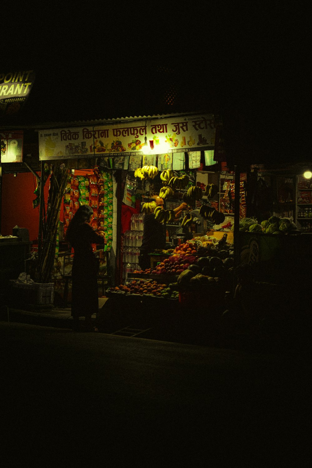 Una persona parada frente a un puesto de frutas por la noche