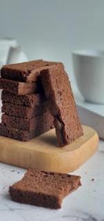 A stack of golden pound cake slices on a rustic wooden board with pastel pink and purple baking tools in the background