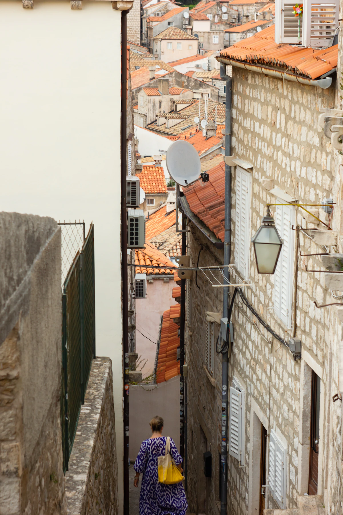 A woman descending a narrow stepped lane between Dubrovnik's limestone houses and red roofs