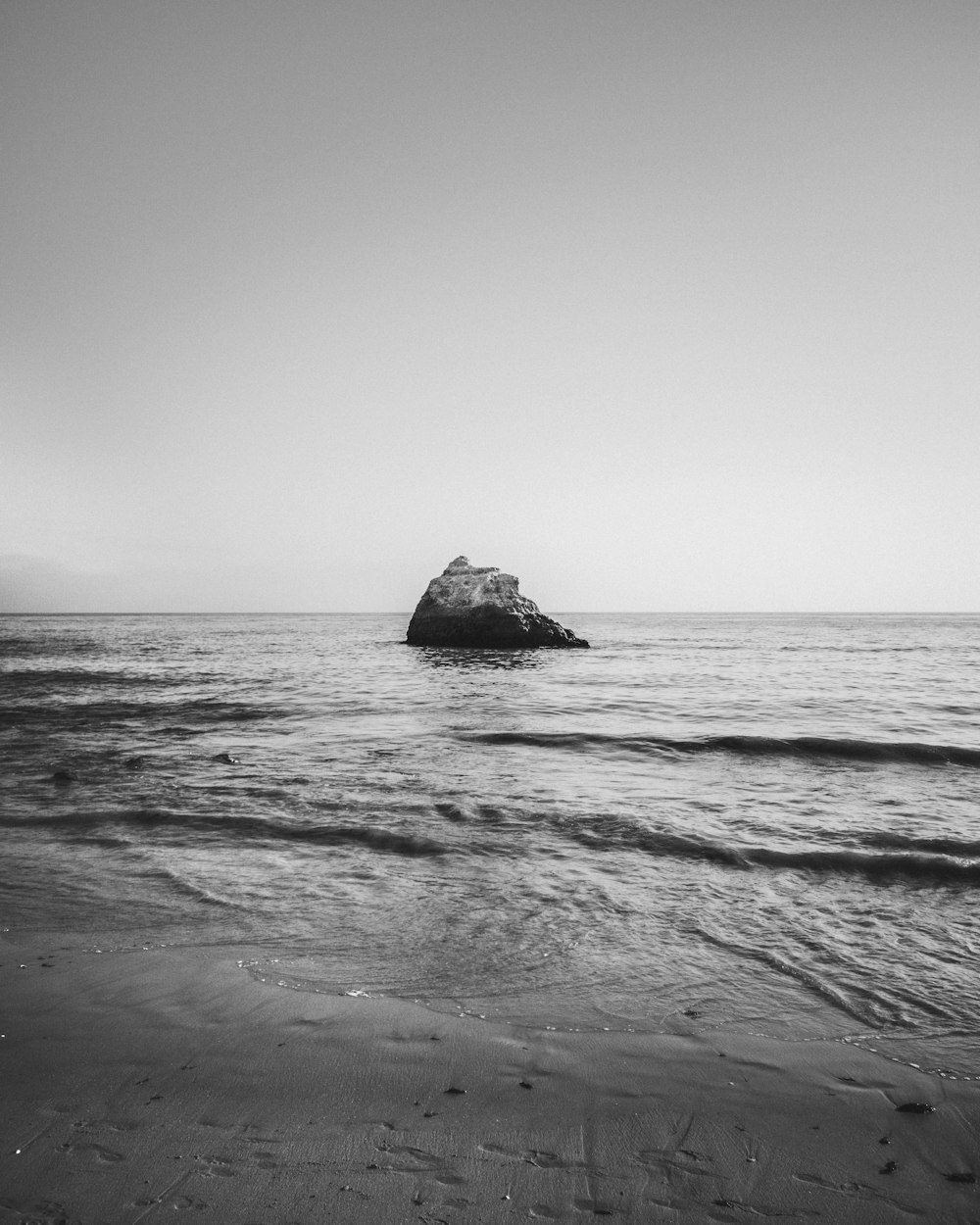 Una foto en blanco y negro de una roca en el océano