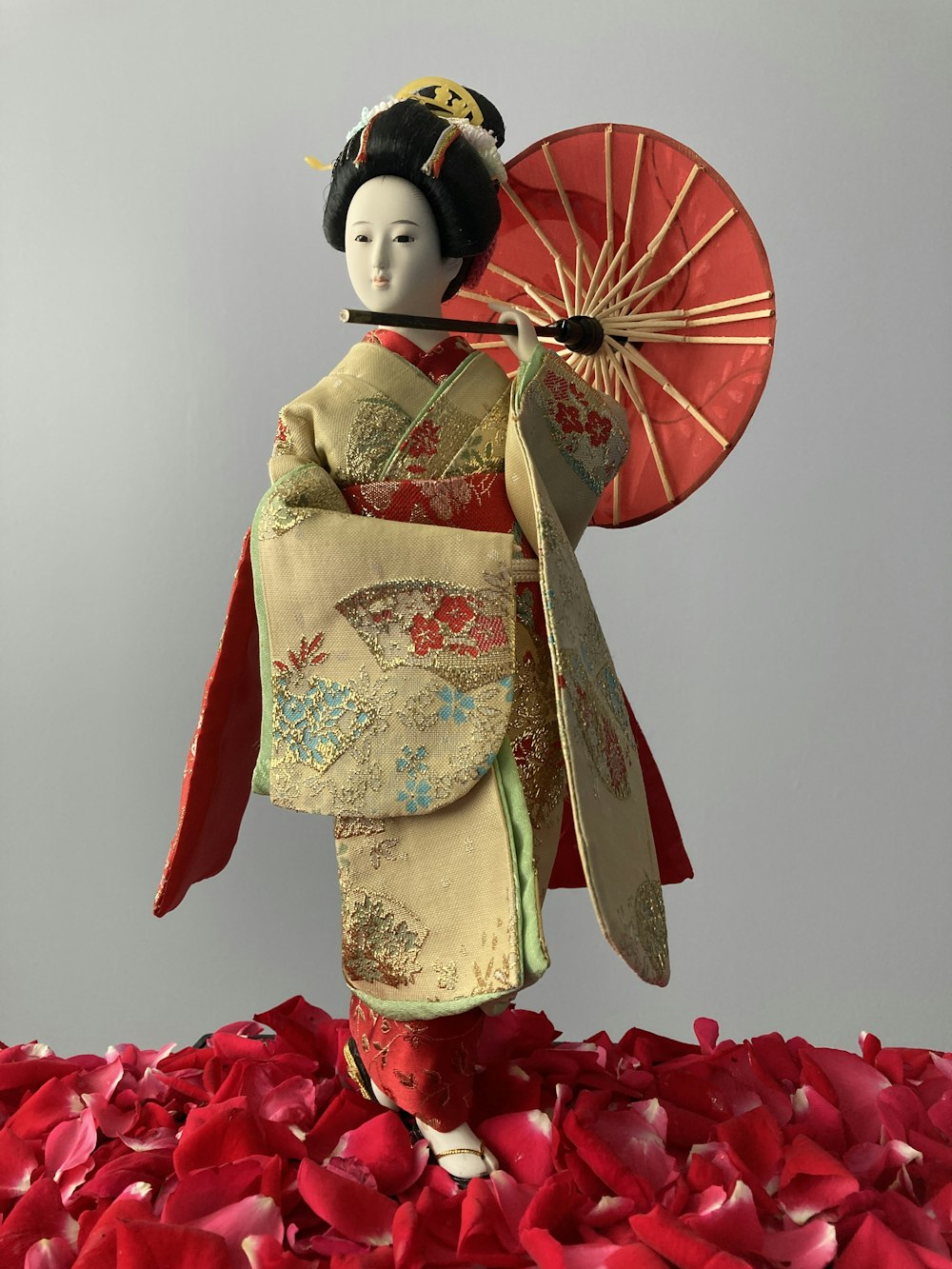 a geisha doll holding a parasol on a bed of petals