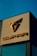 A building facade prominently displays the Cupra logo in metallic tones against a clear blue sky. The sleek, angular design of the logo is positioned above the brand name, also in metallic letters.