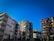 A collection of modern apartment buildings with colorful facades, featuring various shades and materials. The structures are multi-story, with balconies and large windows. The sky is clear and blue, indicating a bright and sunny day.