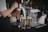 A person is pouring beer from a tap into a glass. Several filled glasses of beer are arranged on the bar counter alongside clean, empty glasses and a damp towel. The scene captures a professional bar setup with a focus on the beer tap system.