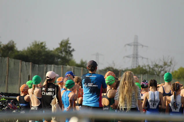 A diverse group of athletes training together outdoors, showcasing swimming, cycling, and running in action.