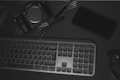 A flat lay of electronic devices and accessories on a dark surface. There is a Sony alpha series camera, a black smartphone, a compact keyboard, and a wireless mouse. A stylus or pen is also visible, and the surface has subtle geometric line patterns.