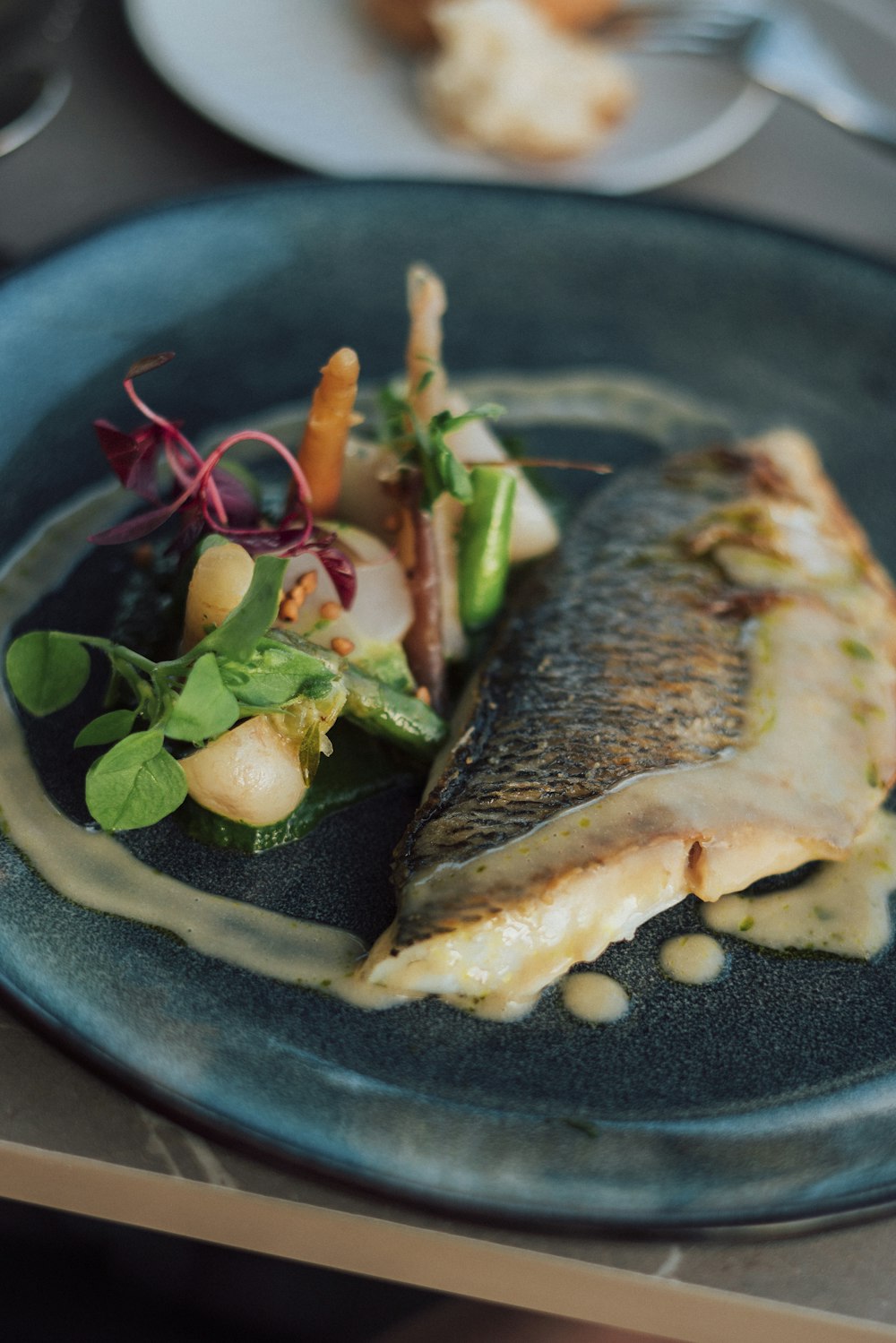 a blue plate topped with a piece of fish next to a salad