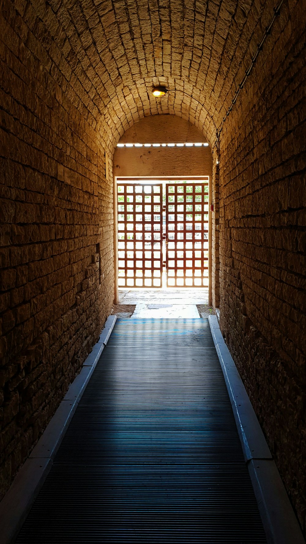a walkway leading into a brick tunnel with a light at the end