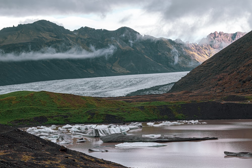 a body of water surrounded by mountains and grass