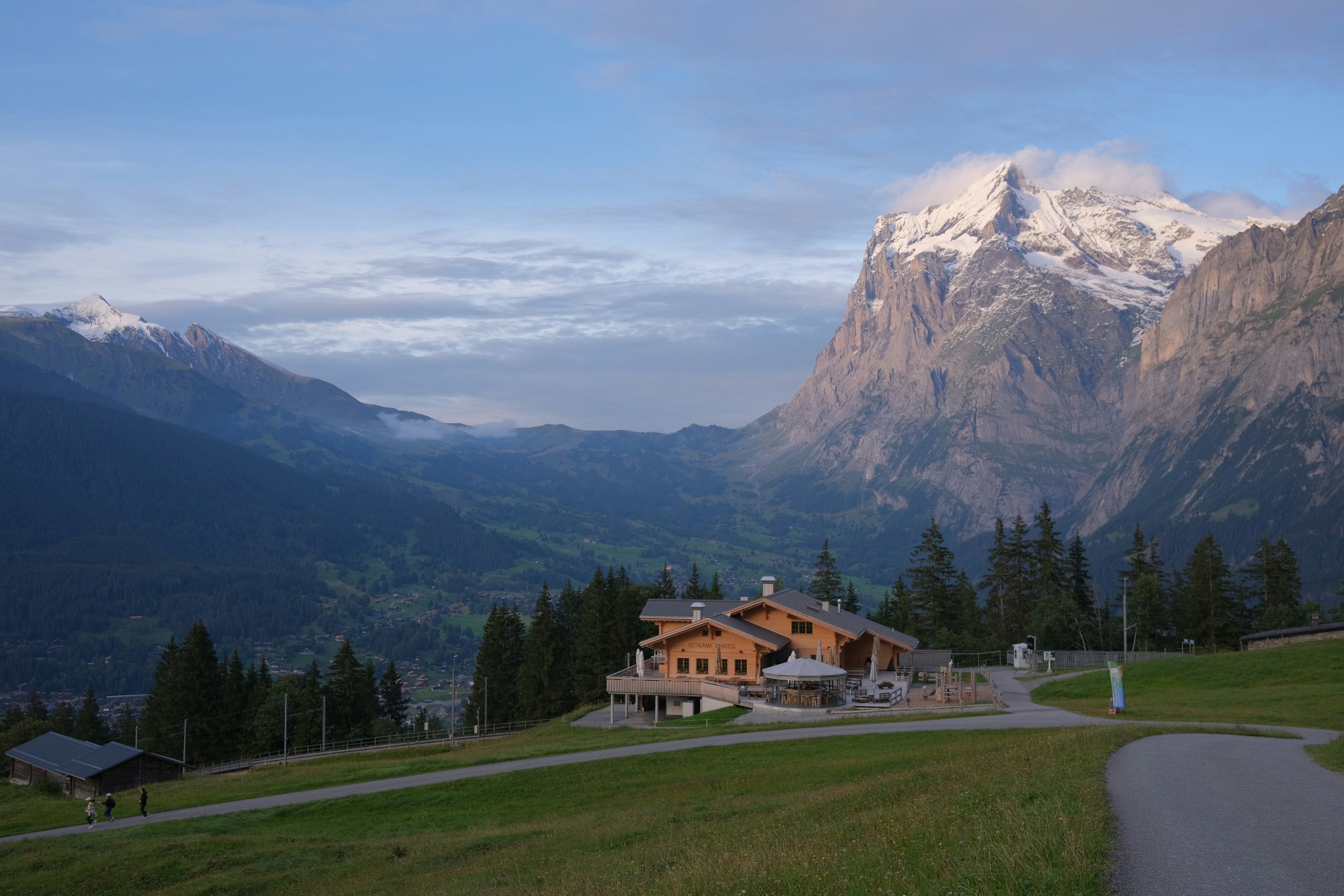 une maison au milieu d’une zone herbeuse avec des montagnes en arrière-plan