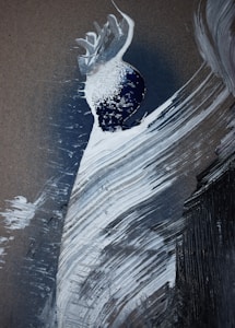 An abstract artwork featuring dynamic brush strokes in white and shades of gray, creating a swirling pattern. A dark blue circular shape with textured white at its top adds contrast, resembling a planet or celestial body.