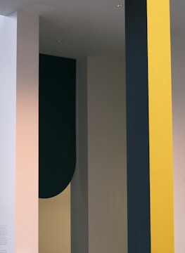 A minimalist design featuring vertical strips and shapes in different colors, including yellow, dark green, and beige. The design has a modern and abstract feel.