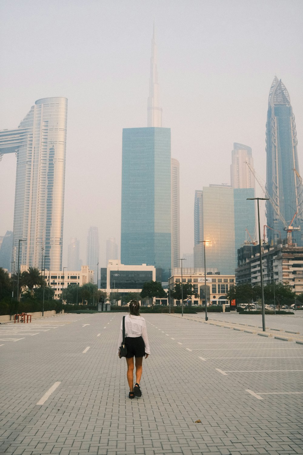a woman walking across a parking lot in front of tall buildings
