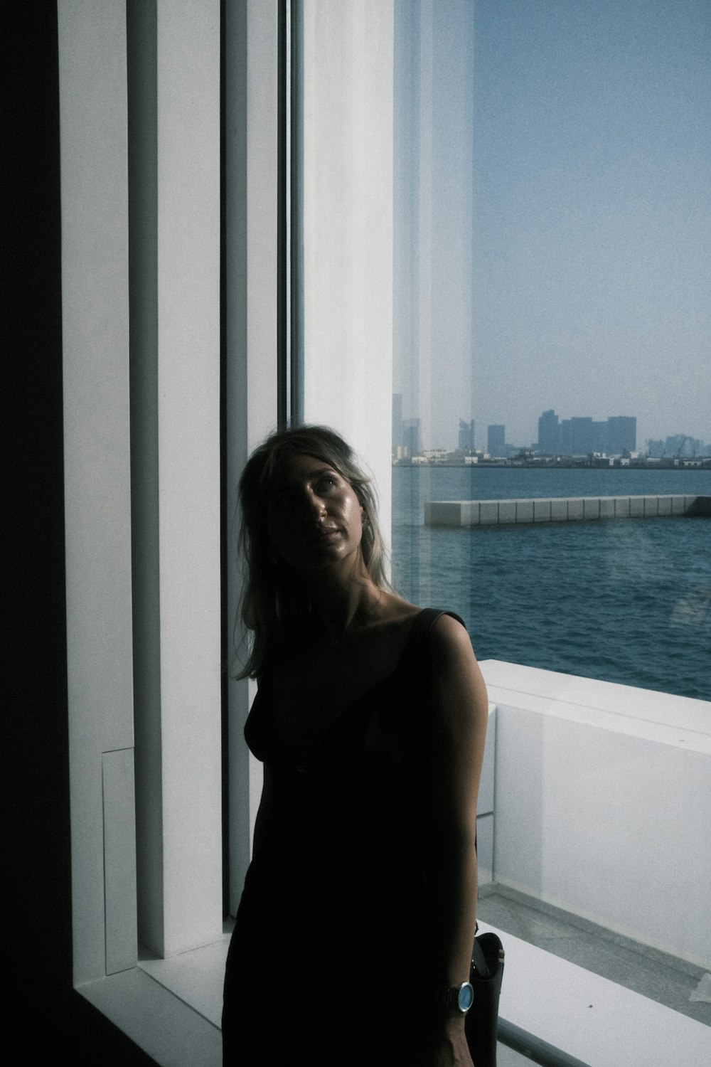a woman standing in front of a window next to a body of water