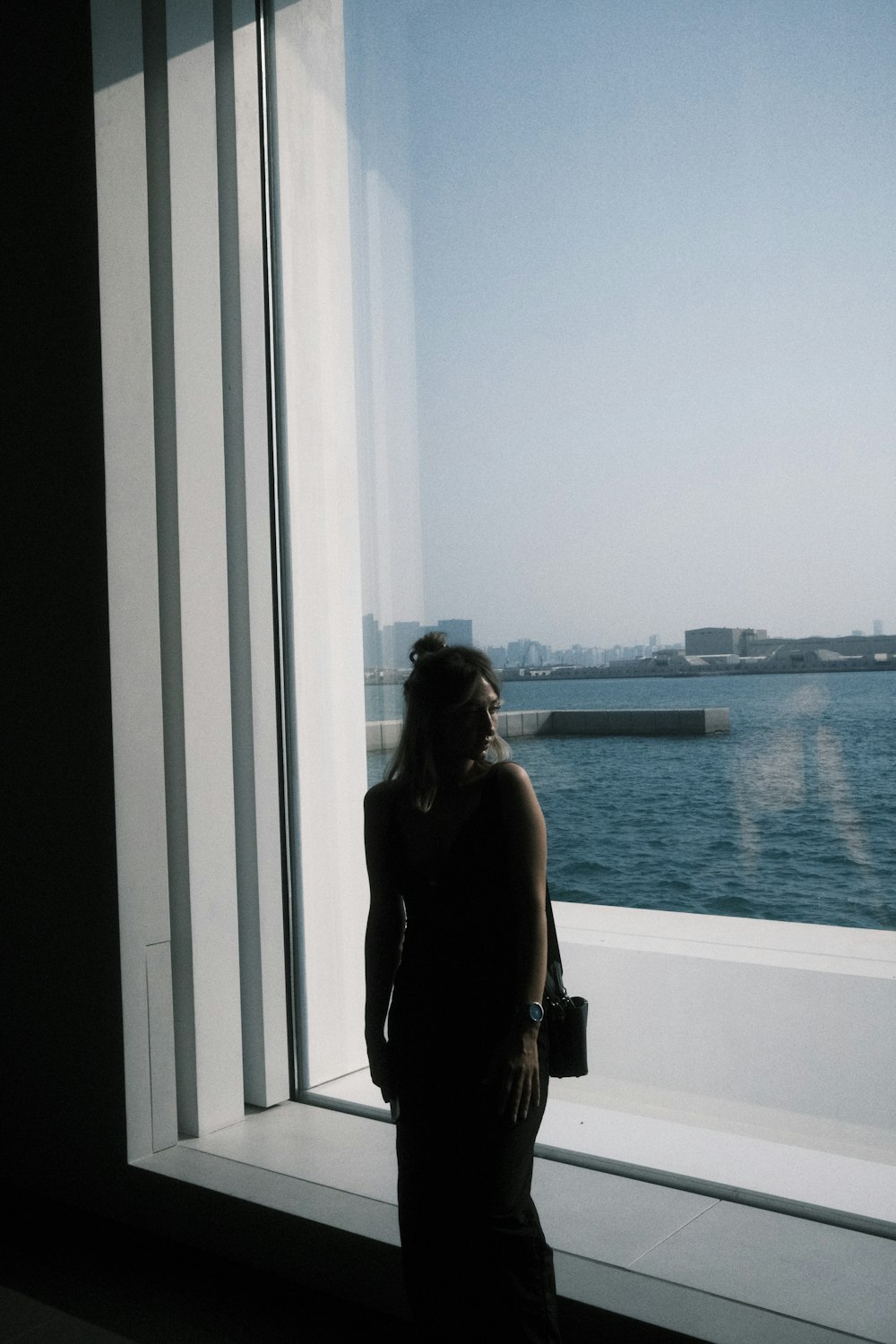 a woman standing in front of a window looking out at the water