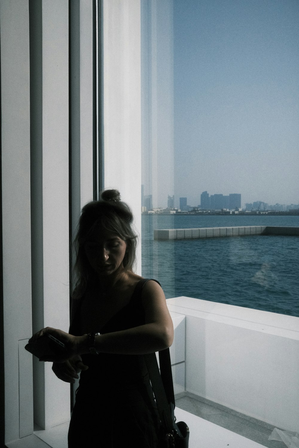 a woman standing next to a window looking out at the water