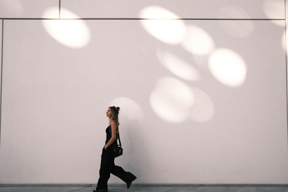 a woman walking down a sidewalk past a white wall