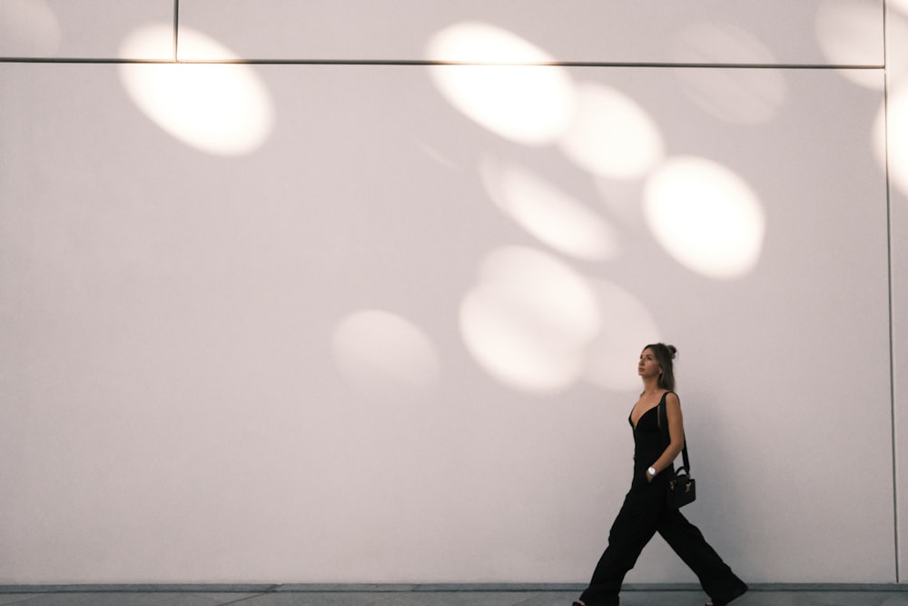 a woman walking down a sidewalk past a white wall