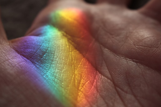A close-up view of a palm with a band of rainbow colors projected onto the skin, highlighting the texture and lines of the hand.
