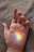 A hand is laid open on a soft, textured surface. A small rainbow is projected onto the palm, displaying a spectrum of colors vividly against the skin.