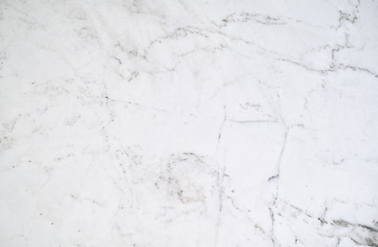 A smooth white surface with subtle gray veining patterns, resembling a marble texture. The image conveys a clean and elegant appearance, with a natural and sophisticated aesthetic.
