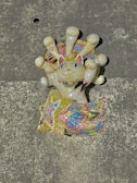 A colorful, intricately designed sculpture of a cat with an ornate tail and crown-like features around its head. The design includes various geometric patterns and bright colors, giving it a festive and artistic look.
