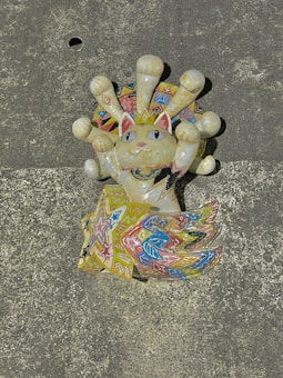 A colorful, intricately designed sculpture of a cat with an ornate tail and crown-like features around its head. The design includes various geometric patterns and bright colors, giving it a festive and artistic look.
