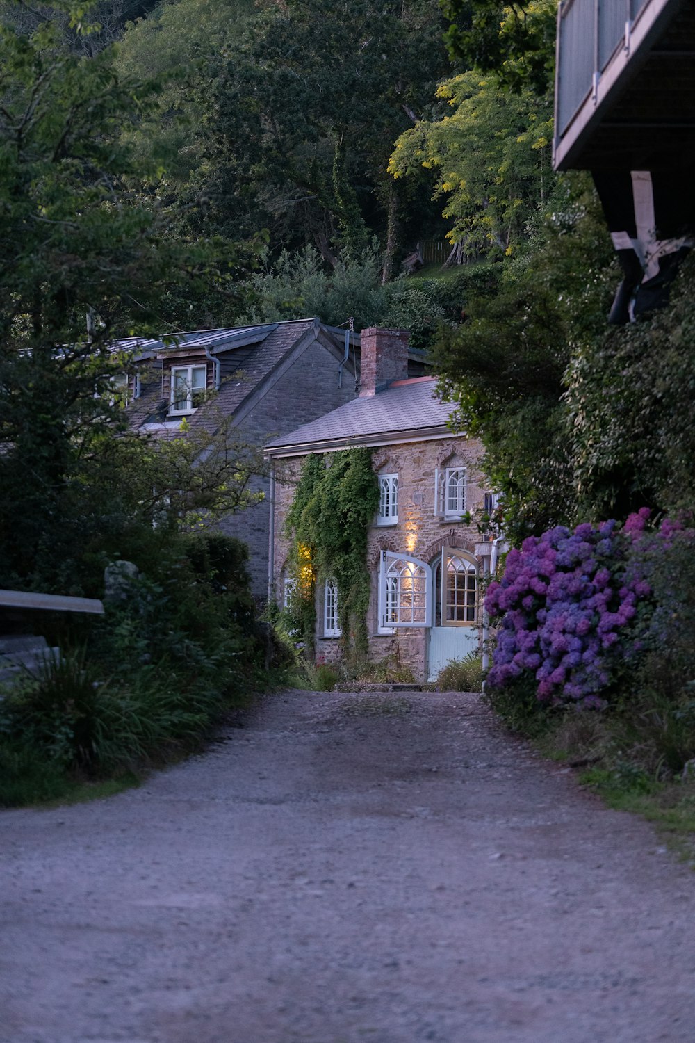 a stone house with purple flowers on the side of the road