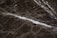 A close-up view of a dark marble surface featuring intricate white veining patterns. The texture appears smooth with a glossy finish. The marble displays a natural, earthy color palette.